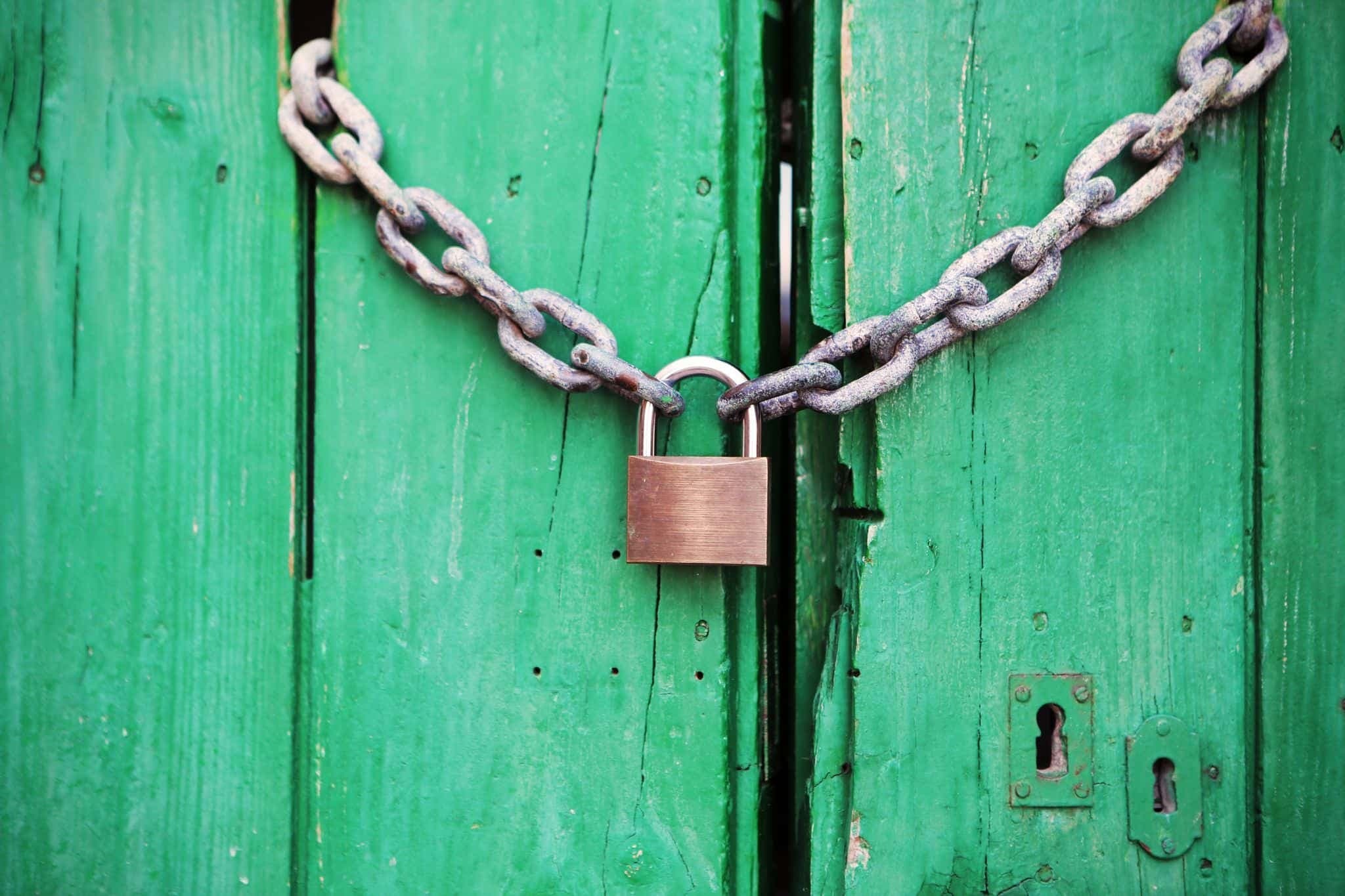 A green wooden door secured with a heavy chain and padlock.