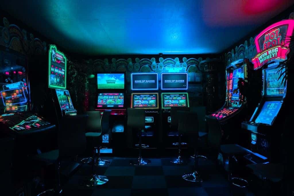 A dimly lit arcade room glowing with neon cabinets and screens.