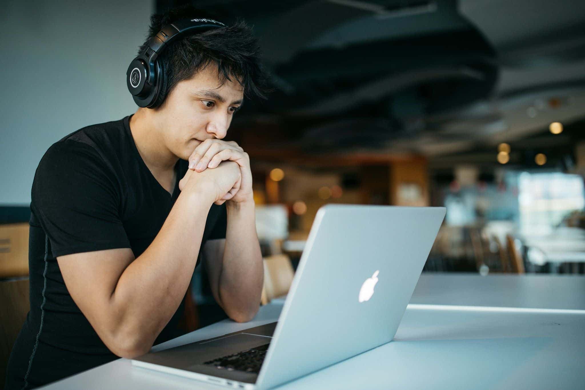 A man wearing headphones speaking at his laptop, practicing aloud.