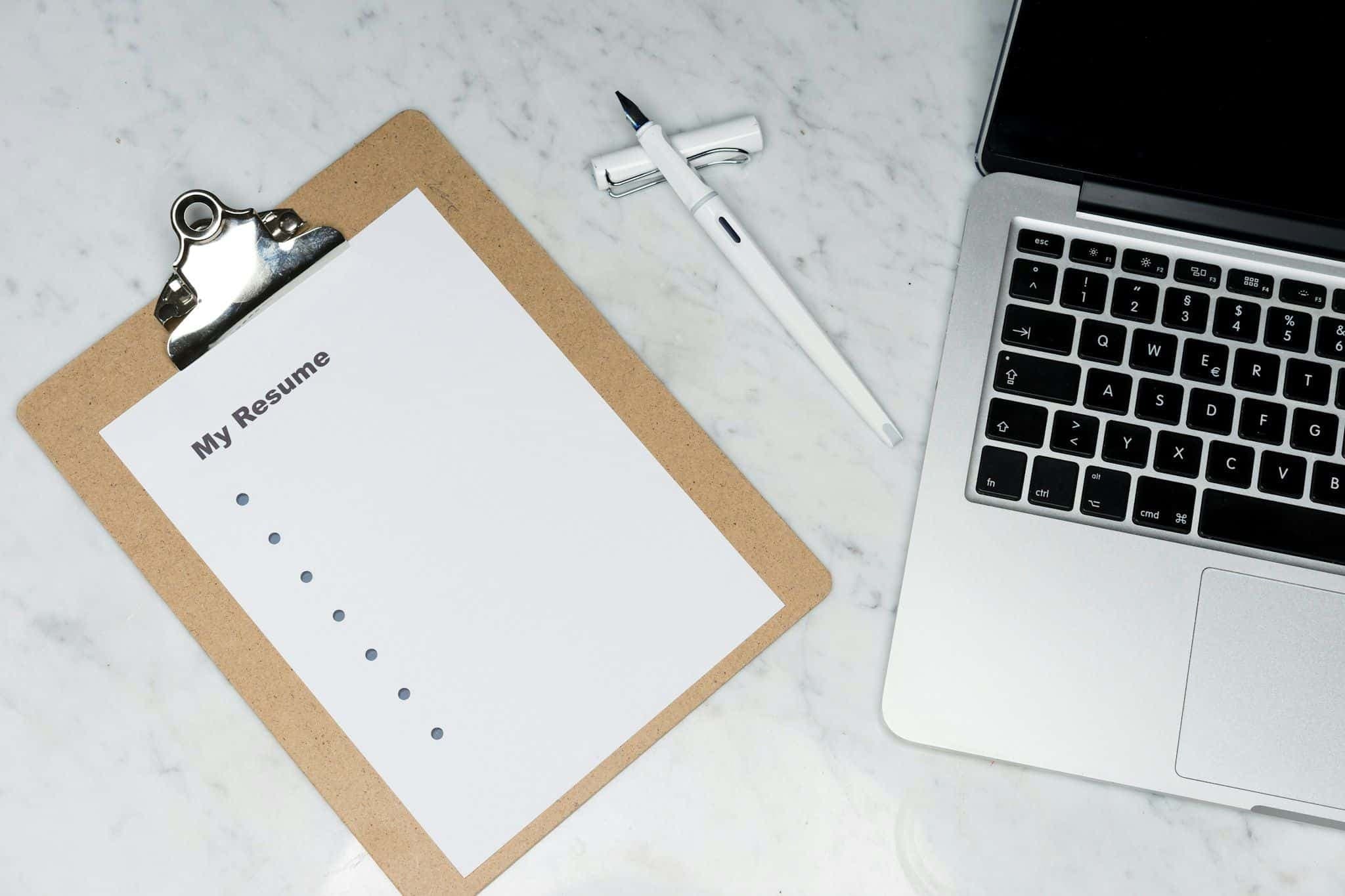 A printed resume on a desk beside a laptop, ready to be tailored for an application.