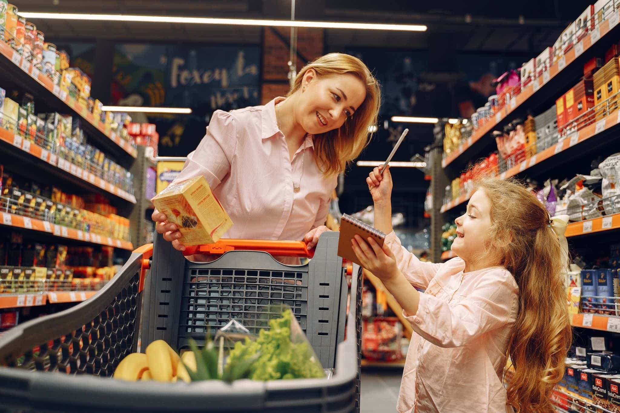 A parent and child shopping in a supermarket with a cart, checking a list together.