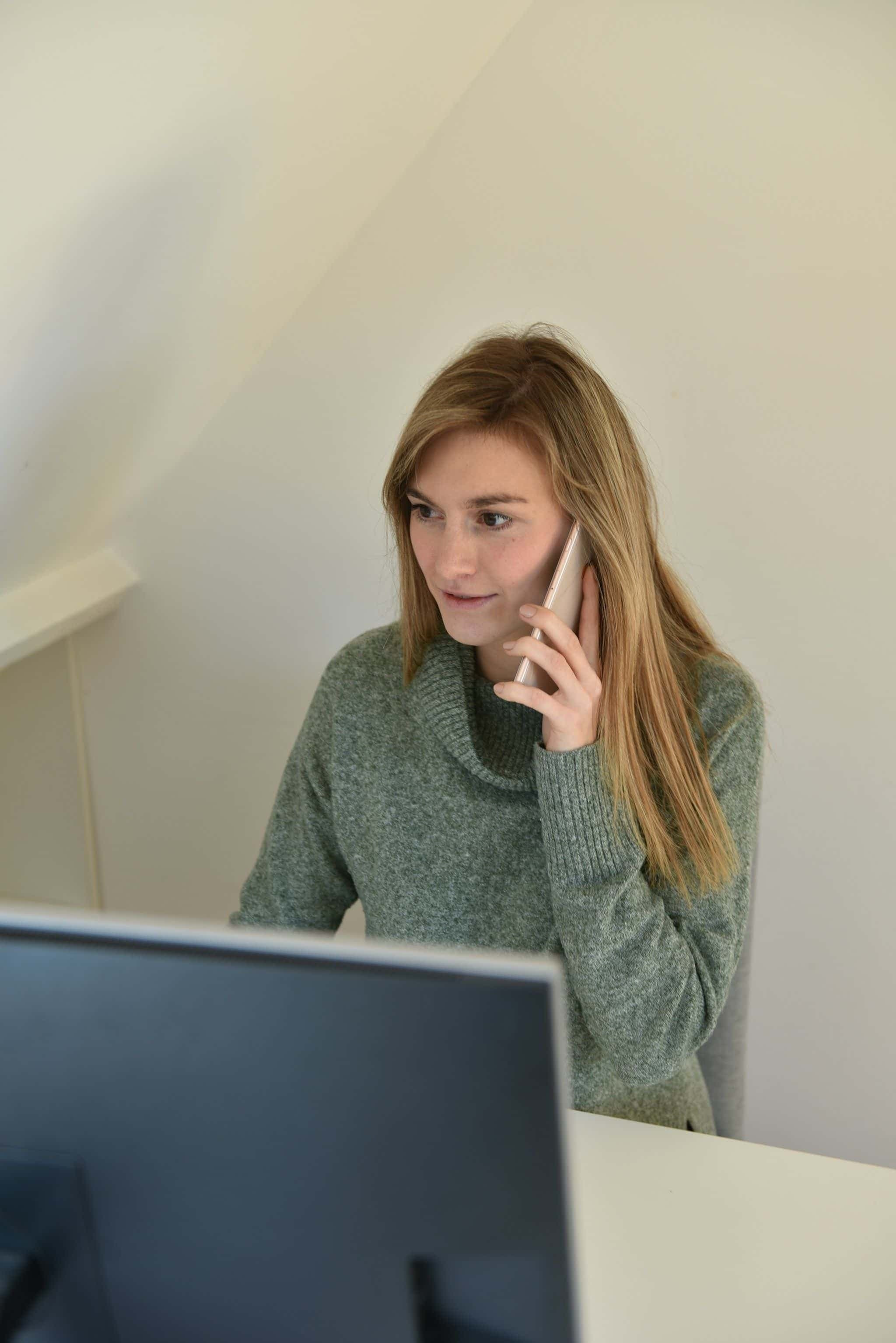 A woman at a desk talking on her phone in front of a computer.