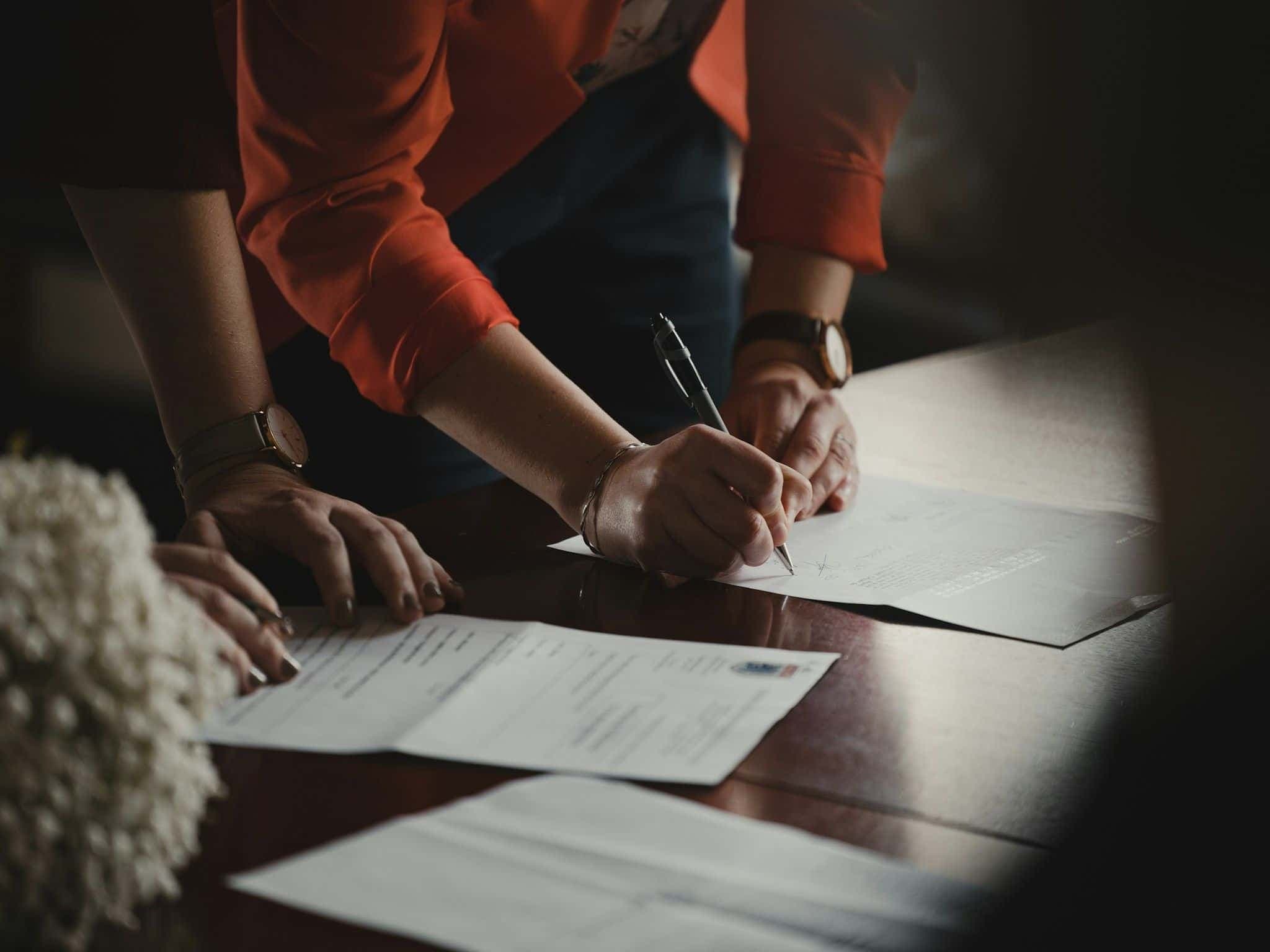 Two people leaning over a table signing paper documents.