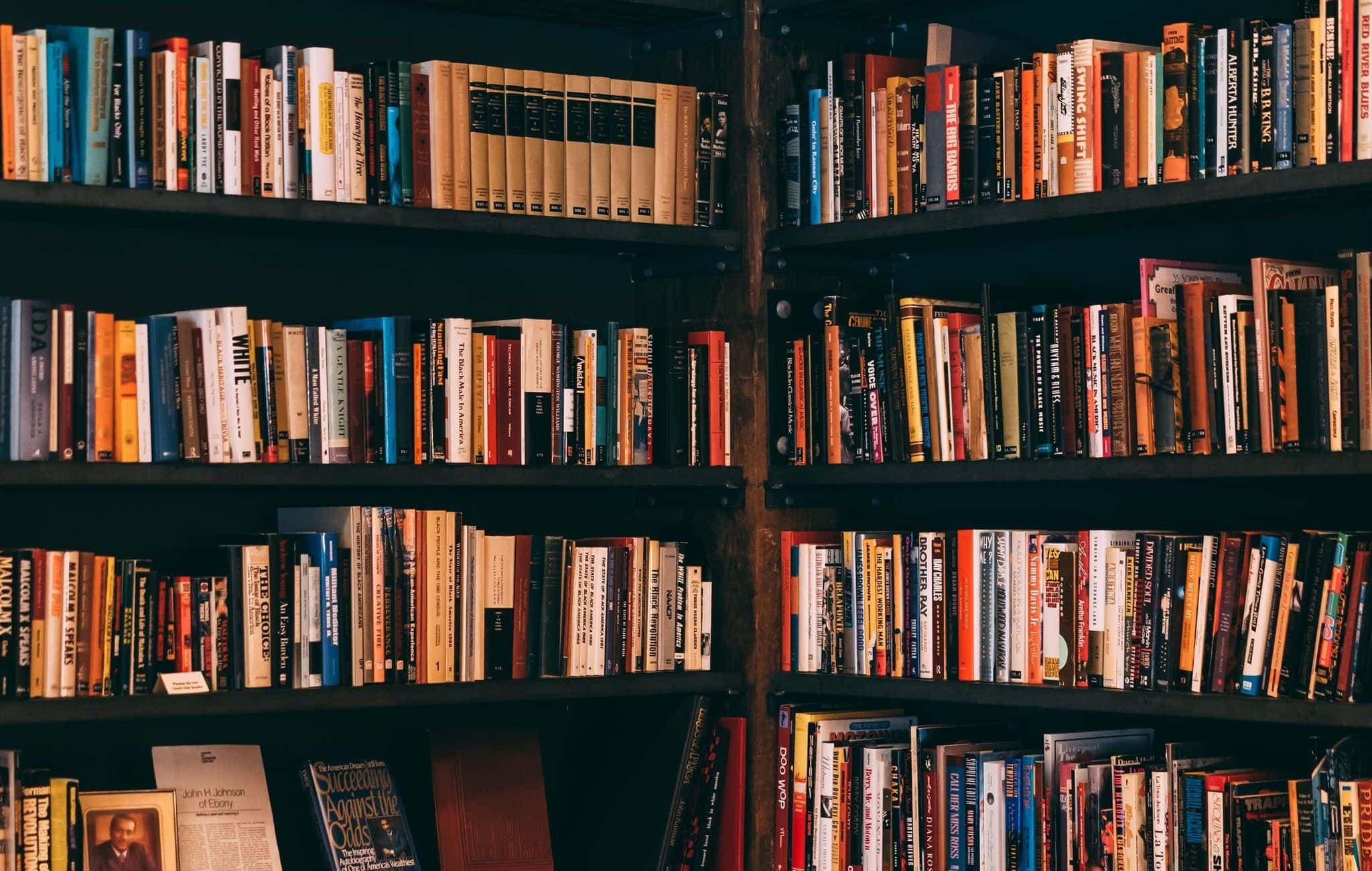 Tall library shelves packed with books, meeting at a corner.