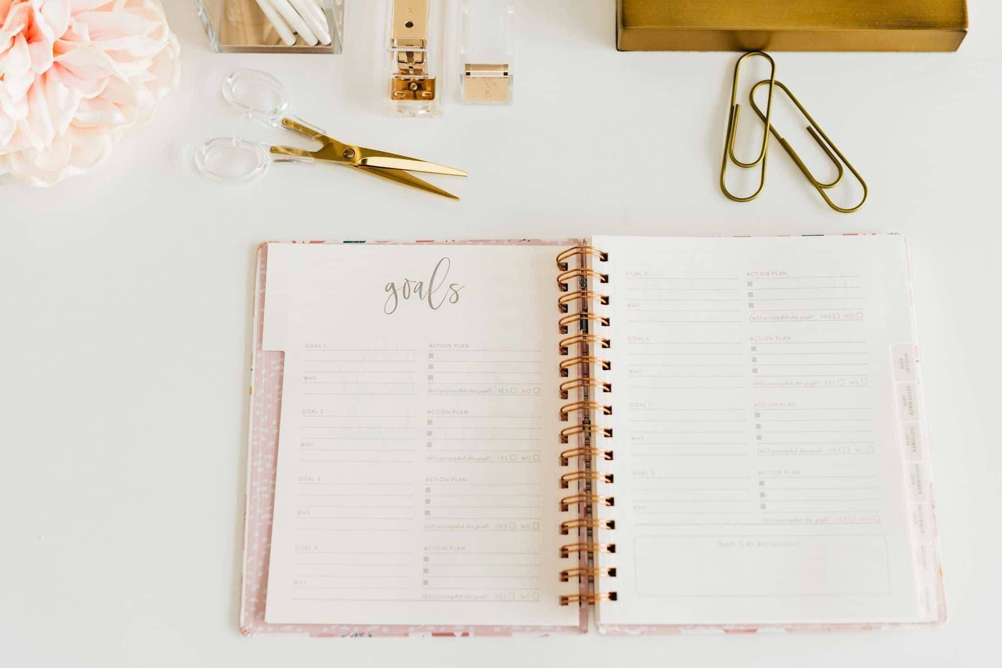 An open spiral planning notebook with scissors and paper clips beside it.