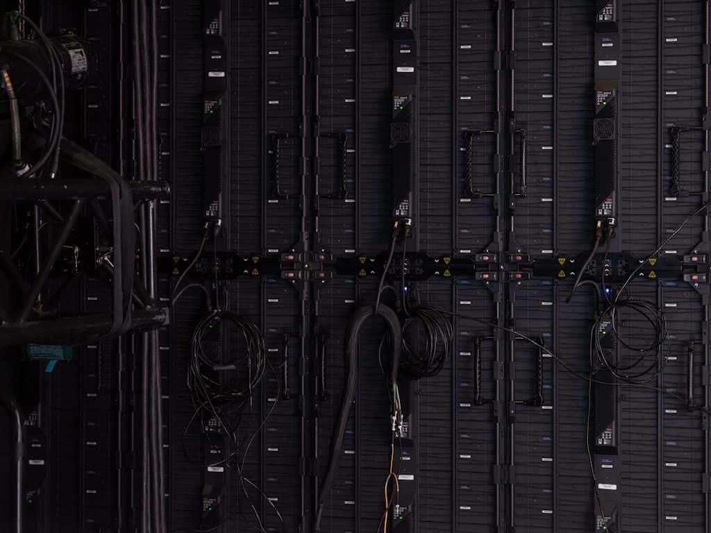 A close-up of dim, blue-lit server racks in a data center, equipment racks receding into the dark.