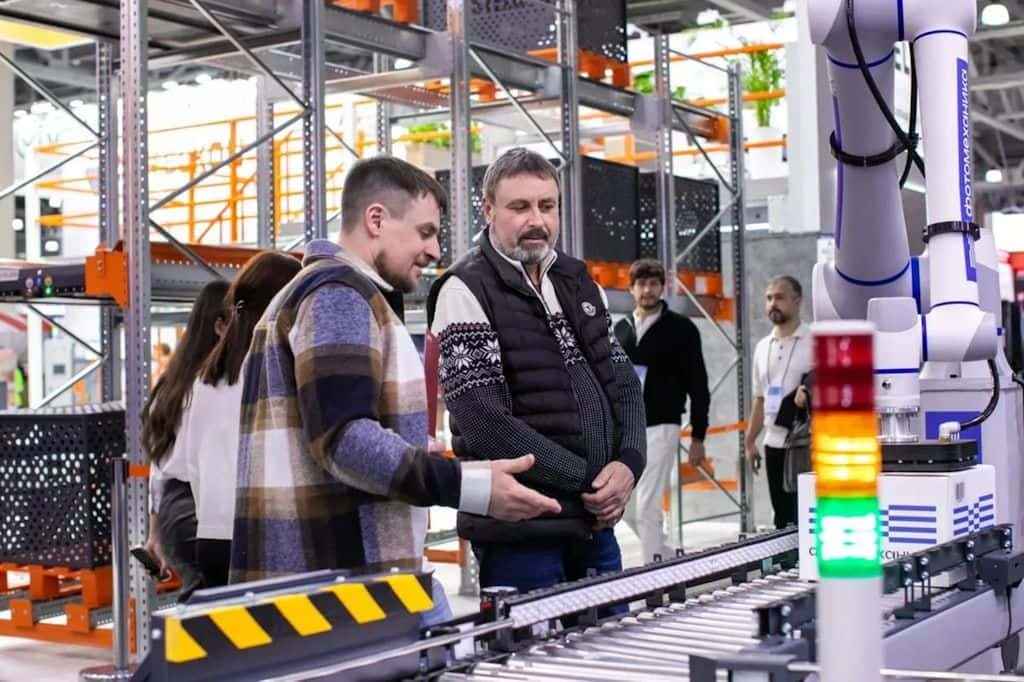 A long industrial conveyor line in a warehouse with metal parts queued in even rows.