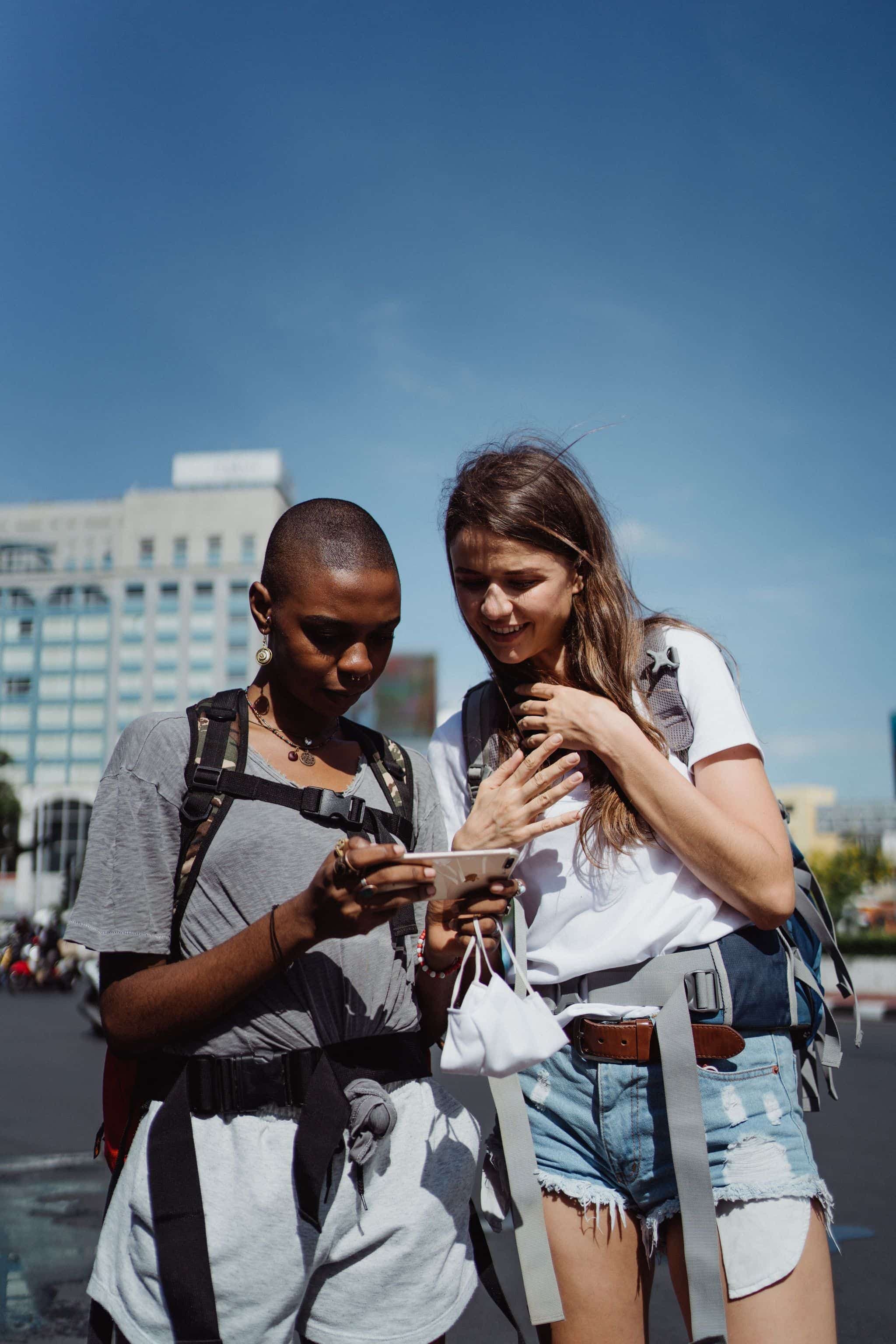 Two travelers on a city street reading something together on one smartphone.