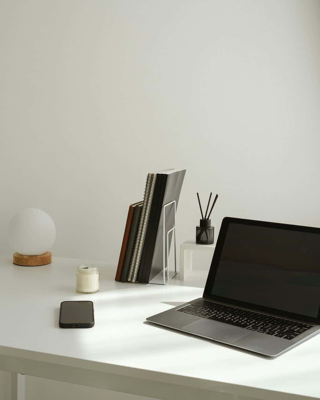 A minimal desk with a single laptop, a phone, and a small stack of notebooks.