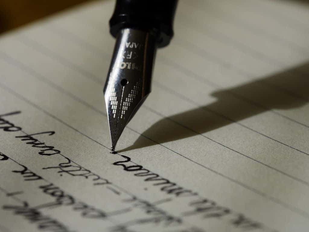 A fountain pen nib touching down on a lined page of handwritten text.