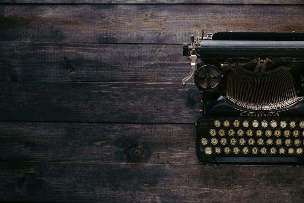 An antique Corona typewriter on a dark wooden table, most of the frame empty wood.