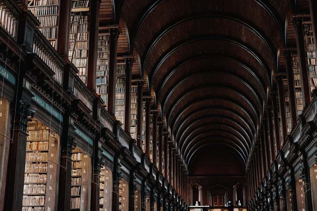 A long, arched library hallway lined floor to ceiling with old books.