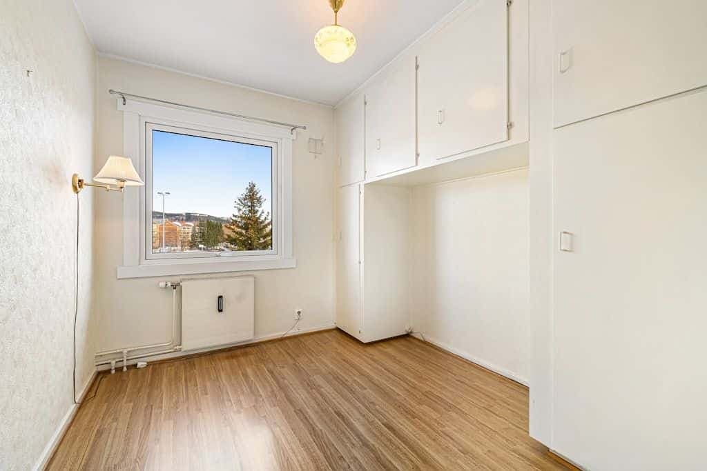 An empty room with hardwood floors, white walls, and a bright window.