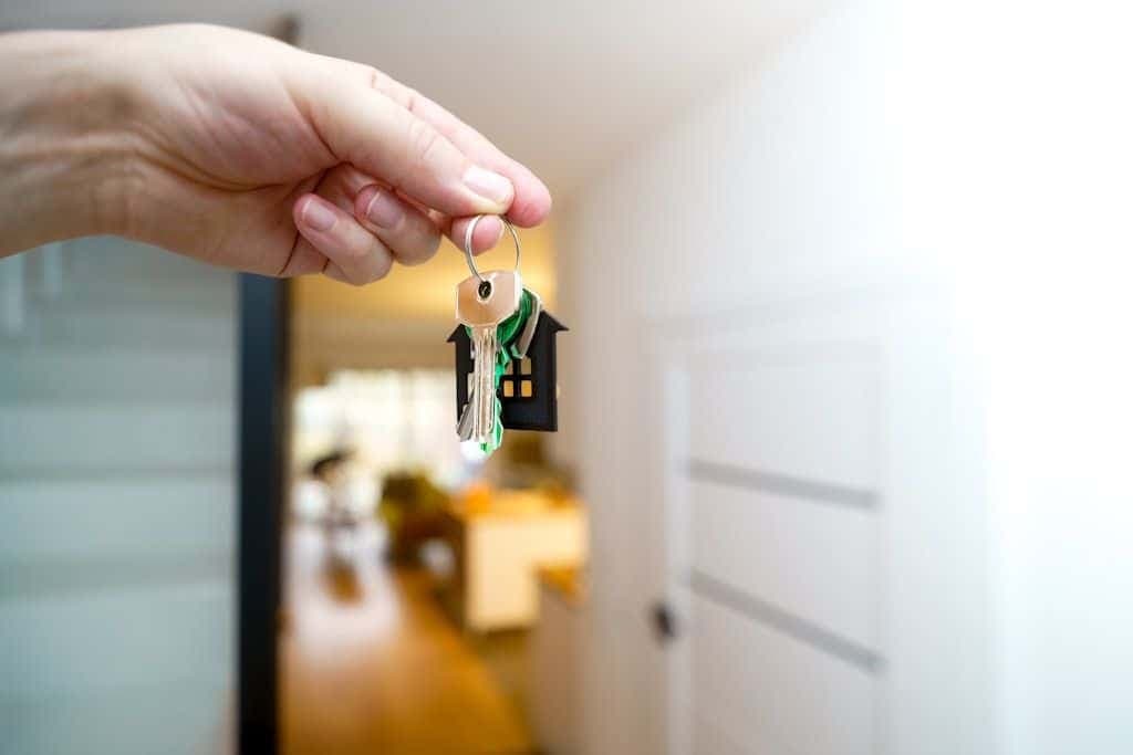 A hand holding house keys in front of a home's entrance.