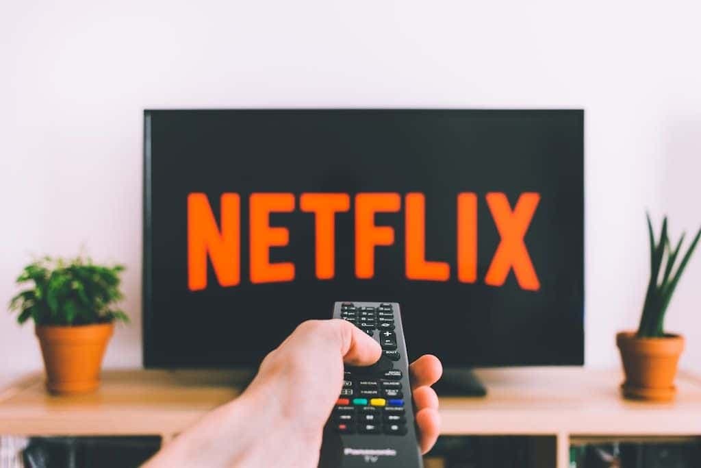 A hand pointing a TV remote at a screen showing the Netflix logo.