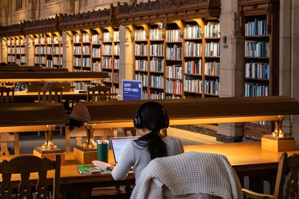 A student studying at a library desk surrounded by open books.