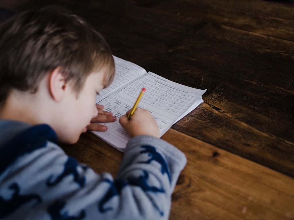 A young student writing in a notebook with a pencil.
