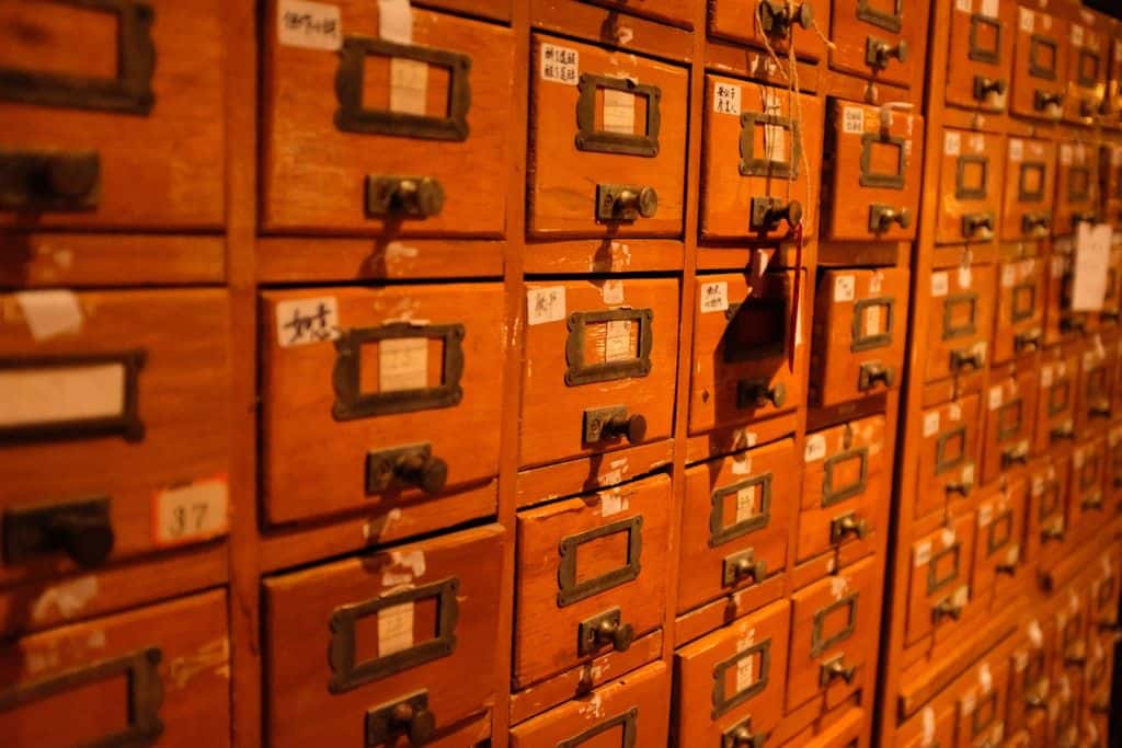 A wall of vintage wooden filing-cabinet drawers with small brass label holders, each drawer indexed by hand.