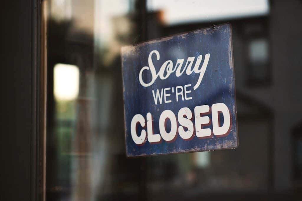 A red and white 'sorry we're closed' sign hanging on the glass door of a small storefront.