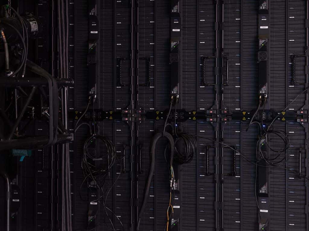 A close-up of dim, blue-lit server racks in a data center, equipment racks receding into the dark.