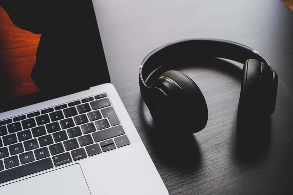 Over-ear headphones resting next to a laptop and a notebook.