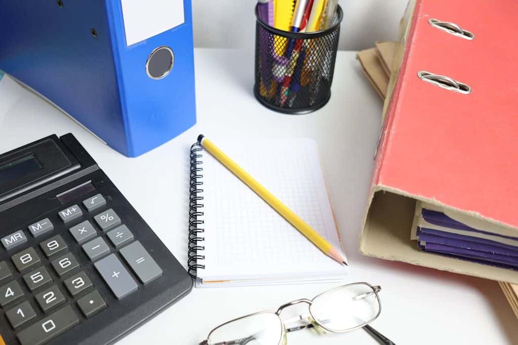 A desk with a calculator, binders, a notebook, and a pair of glasses, set up for budgeting.