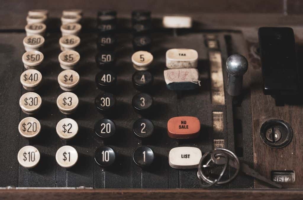 A vintage mechanical adding machine with rows of black and white dollar-amount keys, photographed close-up under warm light.