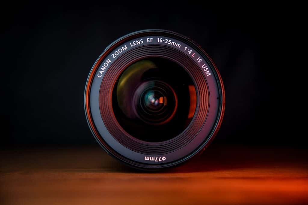 A black camera lens lying on a brown wooden table, side view, shallow depth of field.