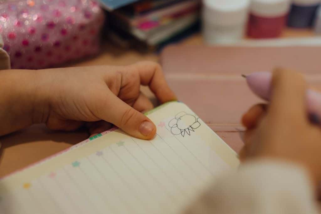 A hand writing in an open notebook on a desk lit by soft purple light.