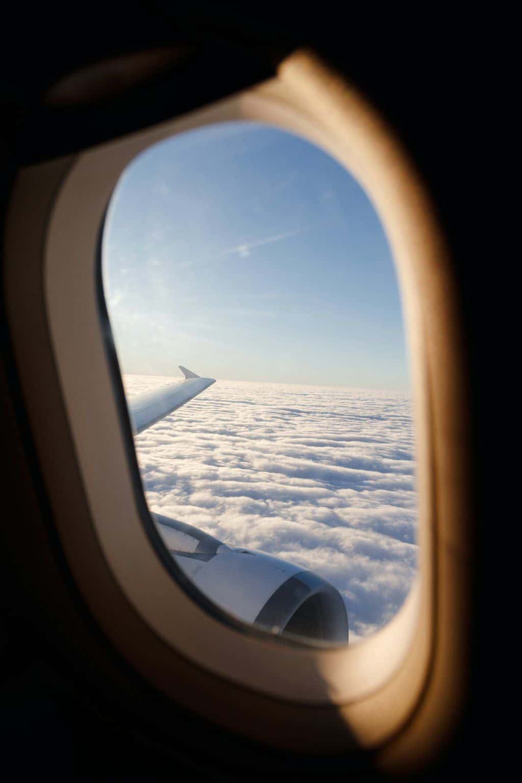 View of soft clouds and a bright horizon through a small airplane window.
