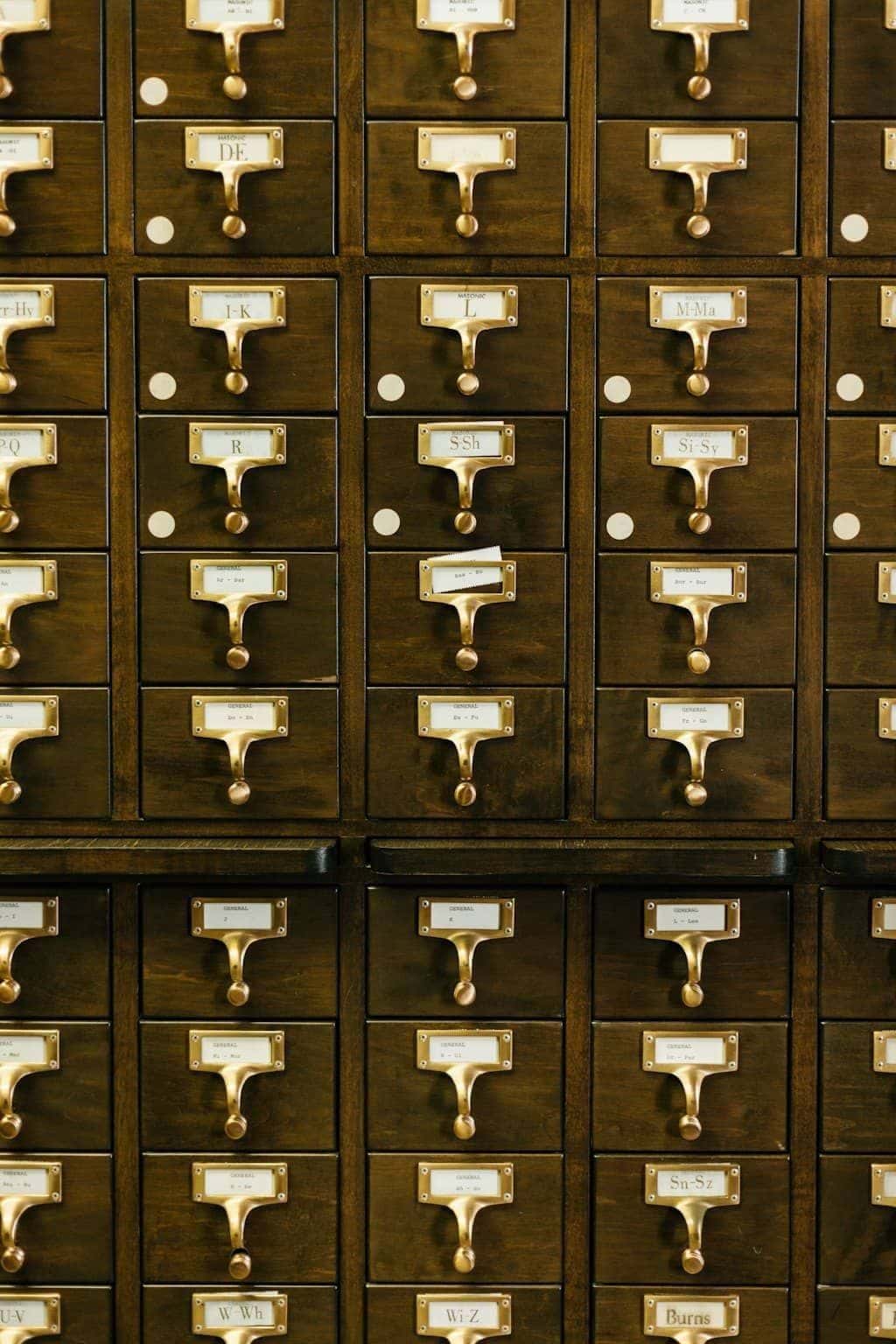 Close-up of a brown wooden library card catalog with labelled drawers stacked in rows.