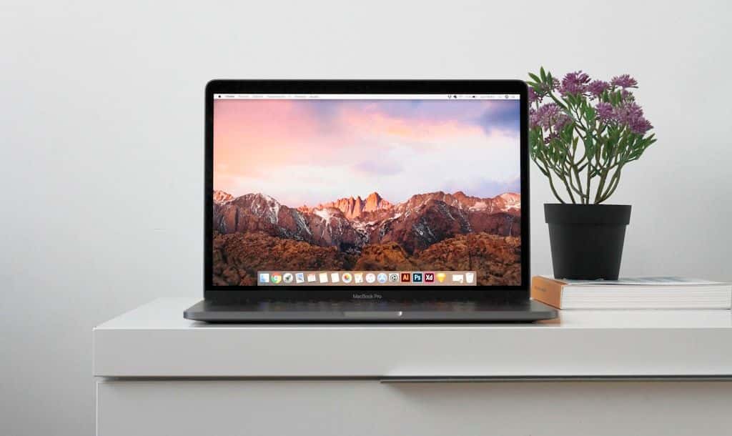 A MacBook sitting open on a clean white table, the screen and dock visible.
