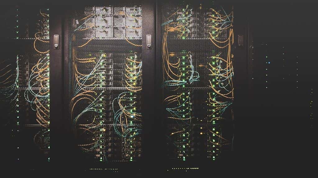 Rows of server racks with dense bundles of network cabling in a data center.