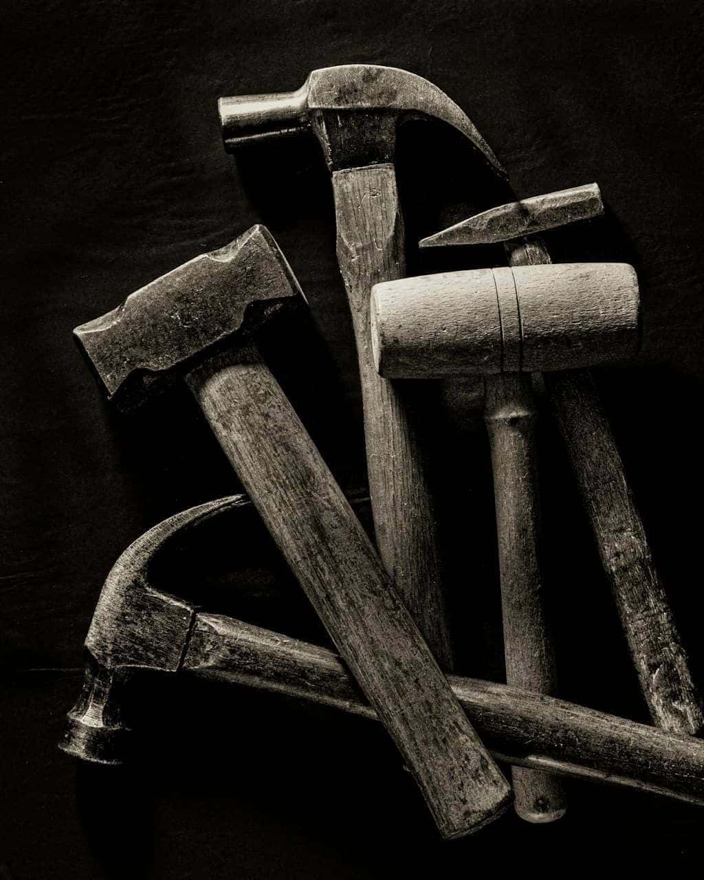 A collection of vintage hand tools — hammers, mallets, a chisel — arranged on a dark workshop background.