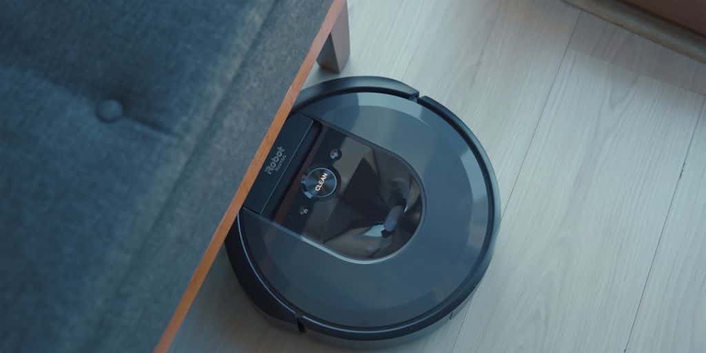 A robot vacuum emerging from under a couch on a wooden floor.