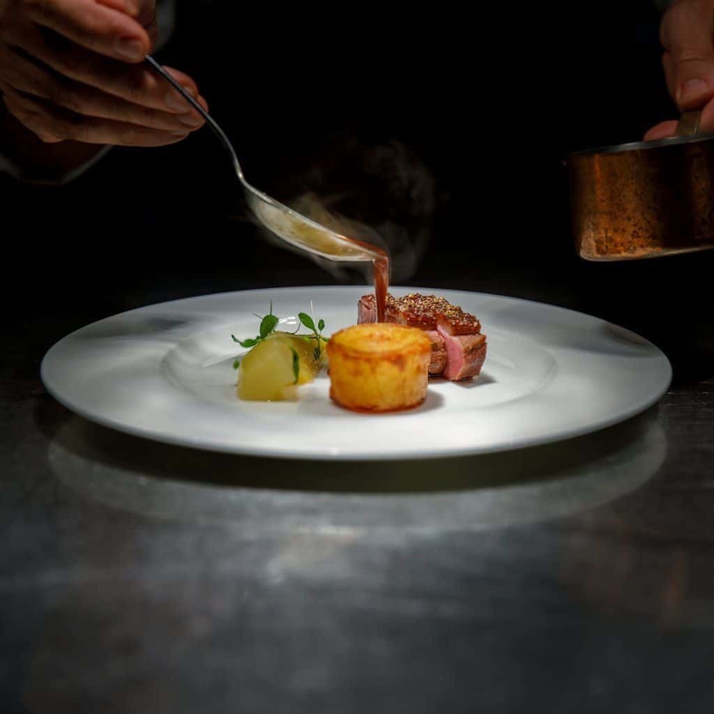 A chef plating a small composed dish at a restaurant pass, narrow focus on the food.